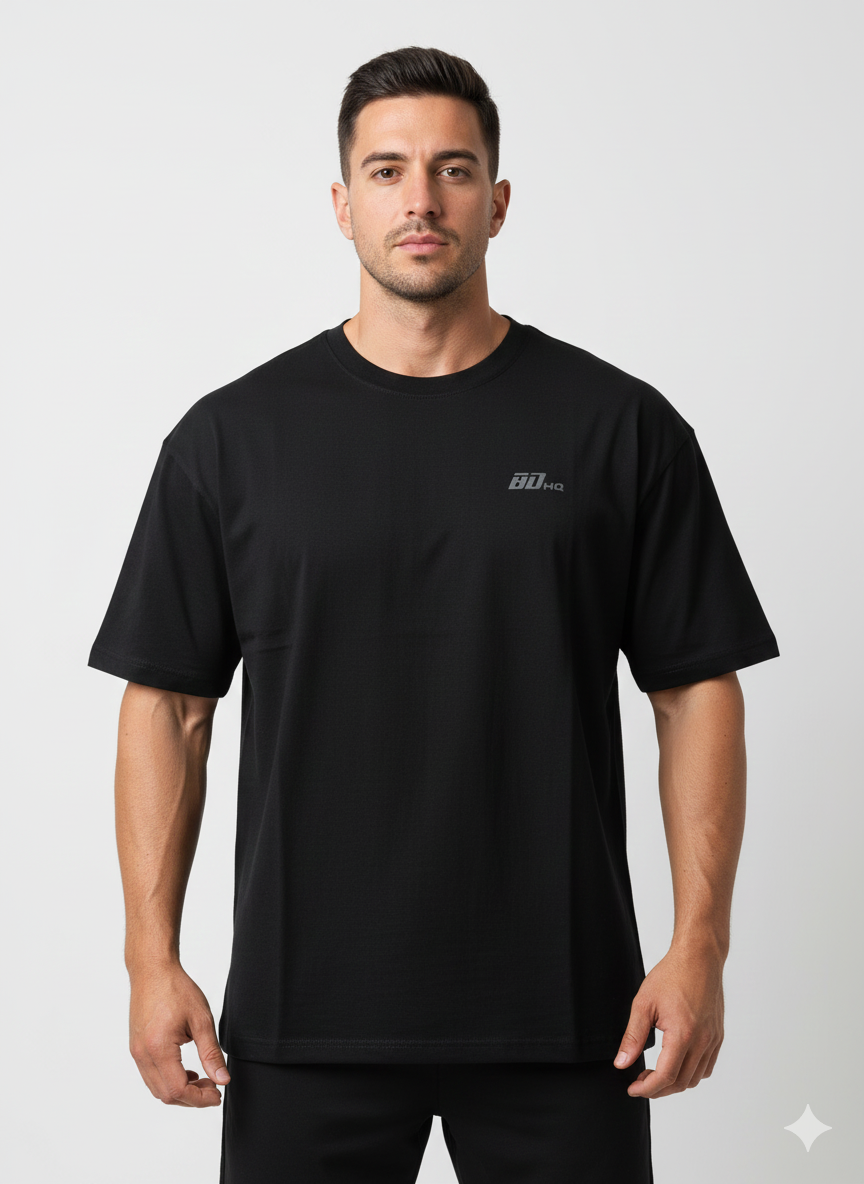 A man stands facing forward against a plain background, wearing the Men's Gym Clothes AU BDHQ Oversized T-Shirt (180GSM) – Lightweight Drop-Shoulder Cut in black with a subtle 90 KG chest graphic.