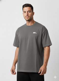 A man wears the BDHQ: Oversized T-Shirt (180GSM) from Men's Gym Clothes AU—a loose-fitting, dark gray, drop-shoulder cotton tee with a small white chest logo—standing against a white background and looking at the camera neutrally.