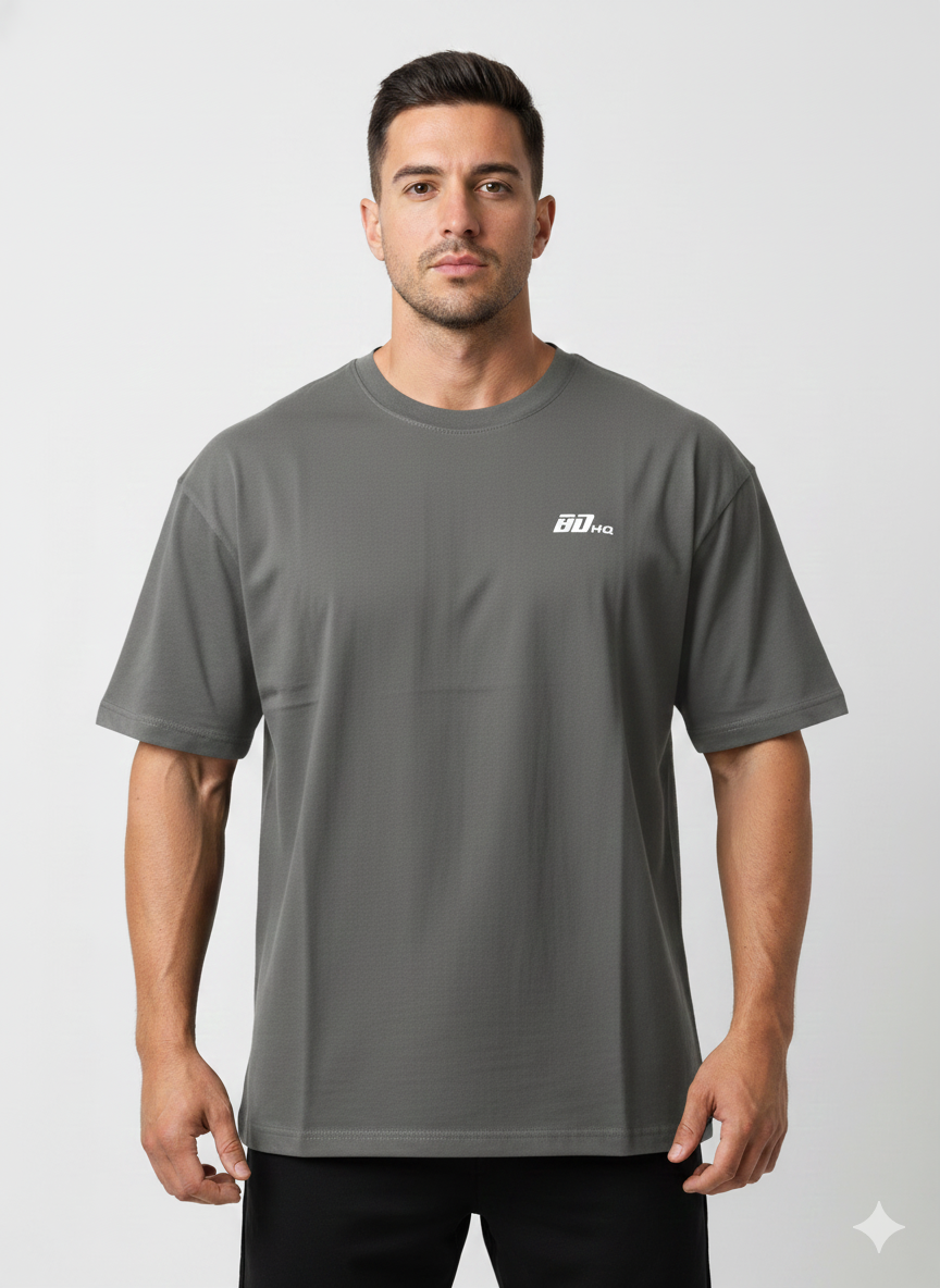 A man with short dark hair and a neutral expression wears the BDHQ: Oversized T-Shirt (180GSM) by Men's Gym Clothes AU, featuring "90 KG" in white on the chest and a lightweight, breathable drop-shoulder design against a plain background.